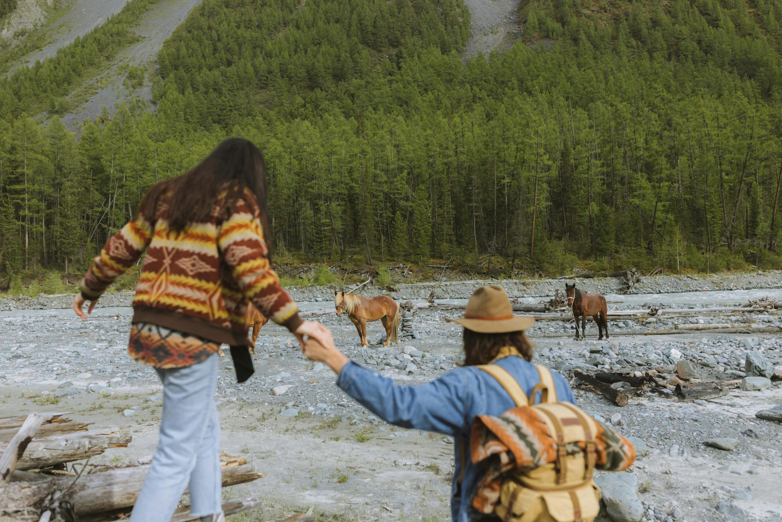 Couple embarked on a scenic hike through a lush forest encountering wild horses by a rocky riverbed.